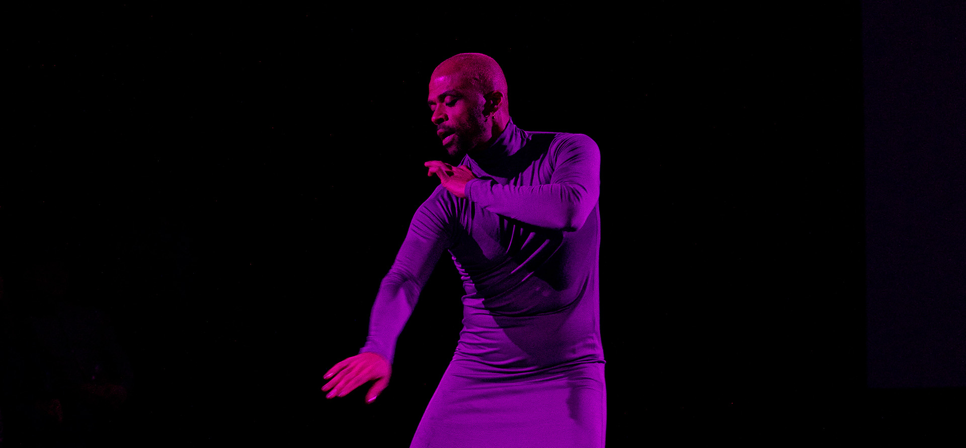 Tummaihoinen mies violetissa mekossa tanssii