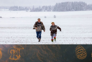 Mies ja nainen juoksevat katsojaa kohti lumisella pellolla, alla syksyistä kuvitusta